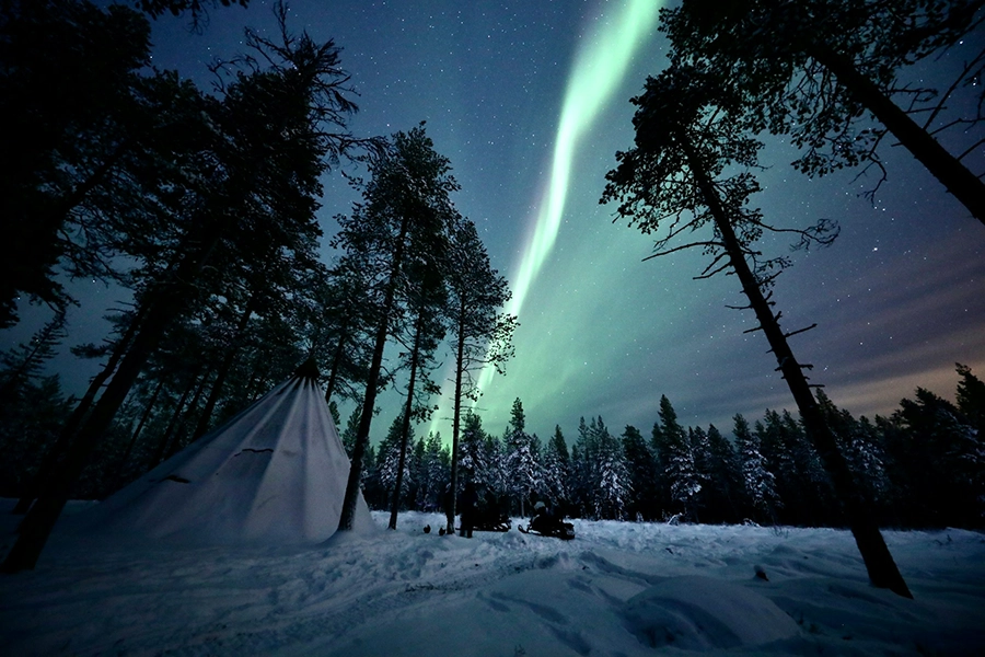 Northern lights dancing in the sky above Rovaniemi Finland with a tee pee style structure in the foreground.